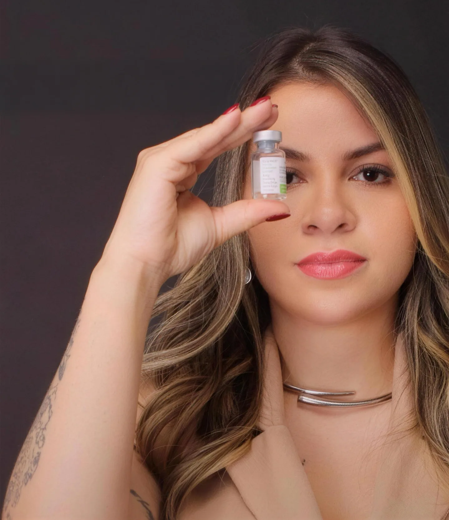 Dra. Débora Moraes de blazer bege, segurando um pequeno frasco à altura do olhar
