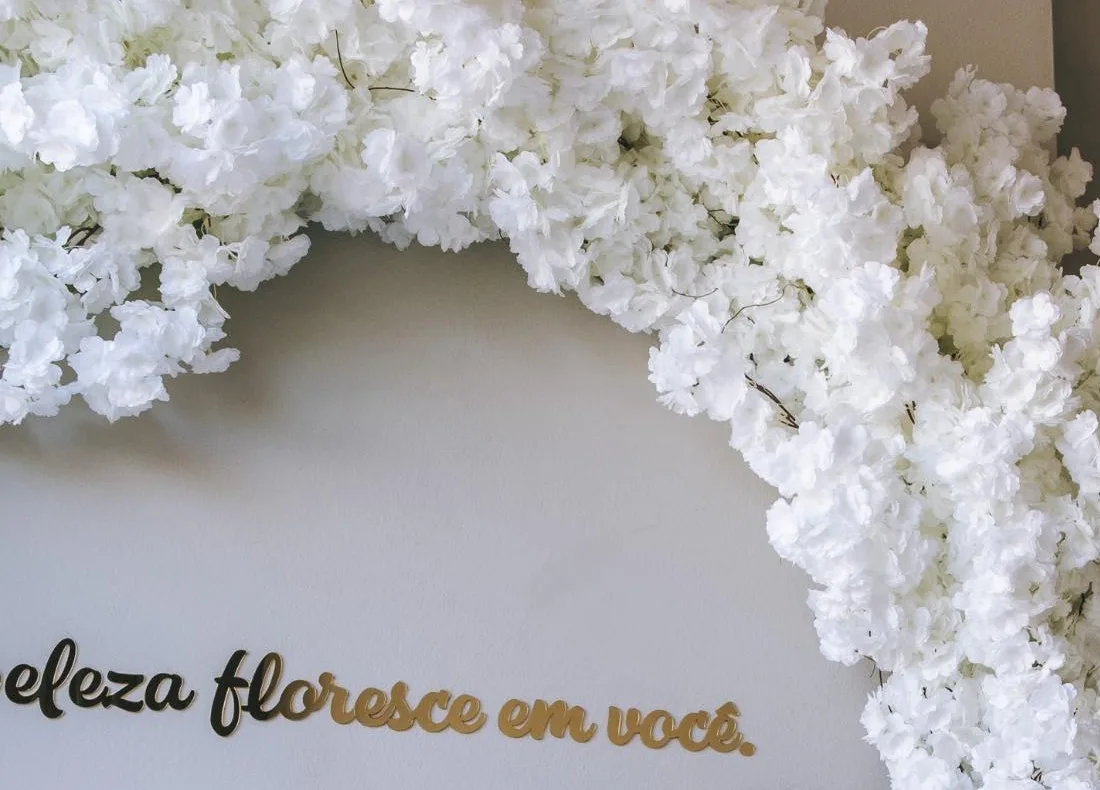 Arco de flores brancas e o letreiro dourado “beleza floresce em você” no Instituto Florescer